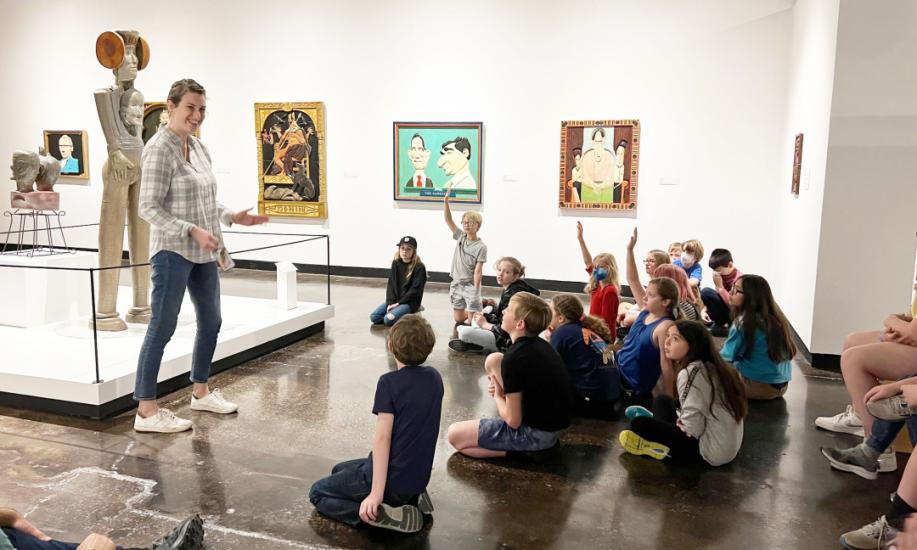 Curator of Art stands in from of a group of children, some raising their hands, seated on the floor in the Lipscomb Art Gallery.