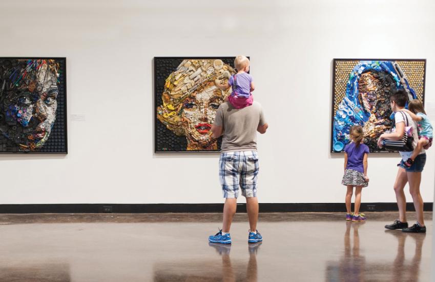 Family looks at 3 pieces of art displayed on a wall, including a portrait of Marilyn Monroe