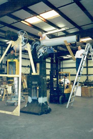 Large white telescope on heavy metal pier with several men on ladders and standing below work on it.