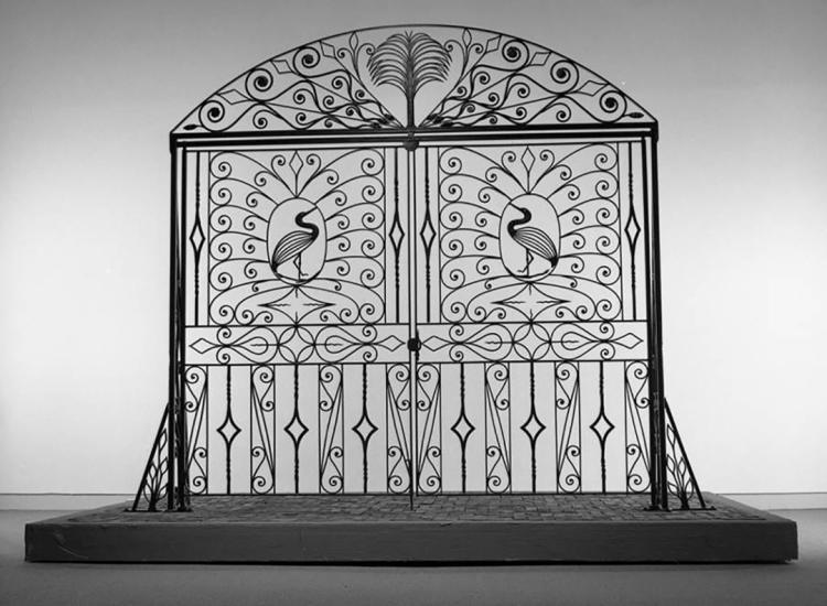 Large black iron gate on display featuring scrollwork and representations of egrets on each side