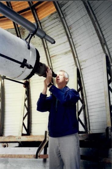 Man in blue shirt looks through eye piece of large white telescope