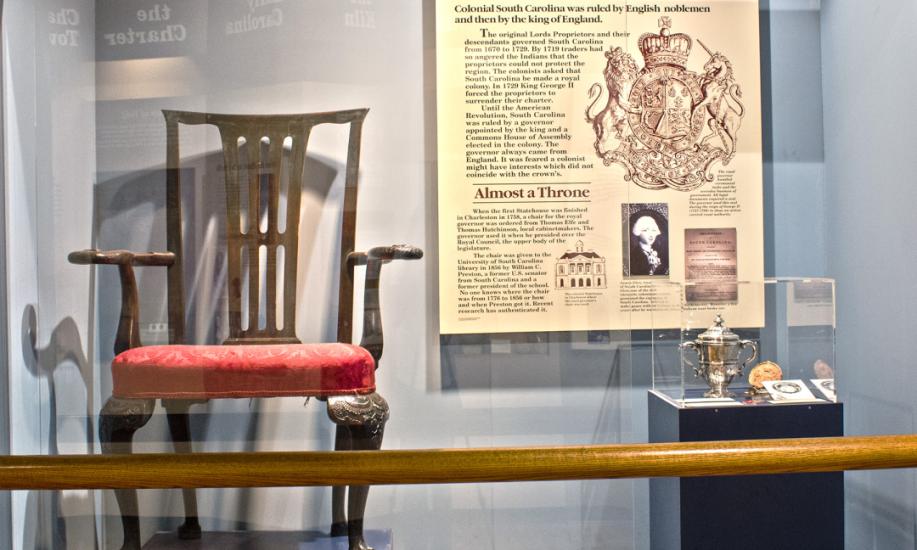 Large, ornate wooden chair with back, arms and scroll feet with red seating cushion