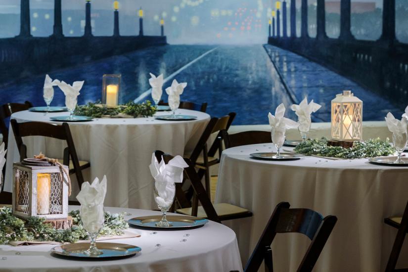 Three formally set table with the white table cloths and napkins with painted mural of bridge in the background