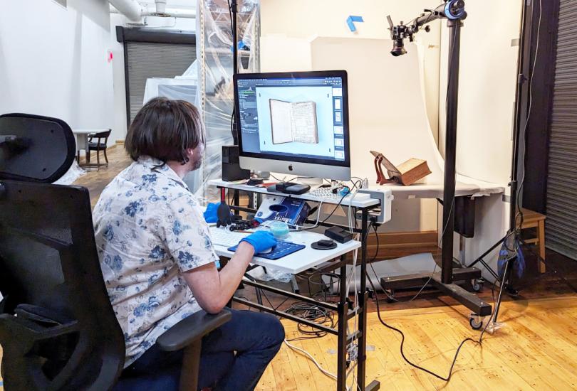Man sits in front of computer with Bible on a table in front of him ready to be photographed.