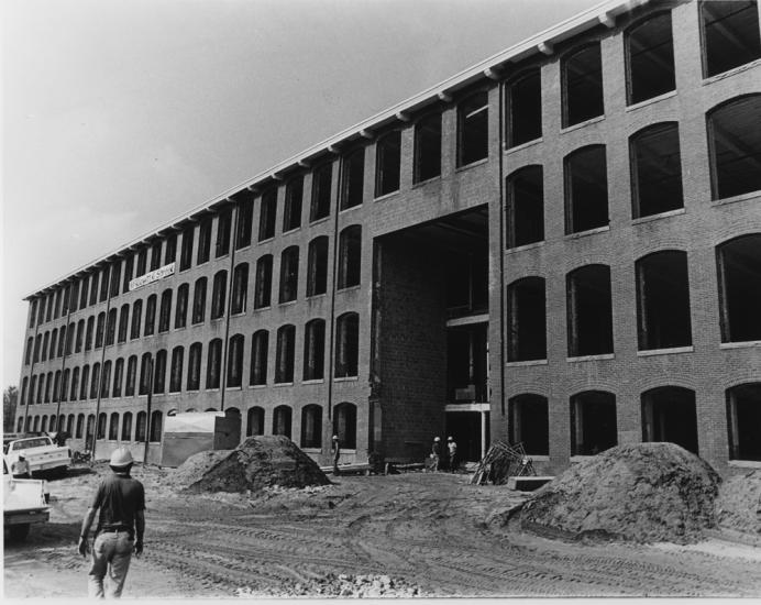 Black and white image of long, four story textile mill building under renovation. An man in a hard hat is visible in the lower left corner.