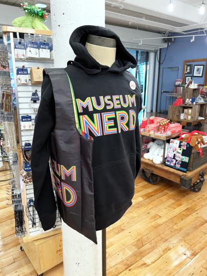 Display Mannequin Wearing a Black hooded Sweatshirt and Black tote bag that both read in multi colored lettering Museum Nerd