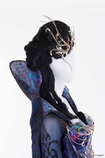 Mannequin in profile on white background with dark wig wearing Twisty and spiked metal crown and a purple and gold dress