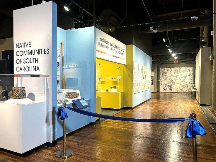 Wall that reads" Native Communities of South Carolina." Several display cases are visible as well as bright yellow alcove with a sign above that reads: Traditions in Catawba Clay