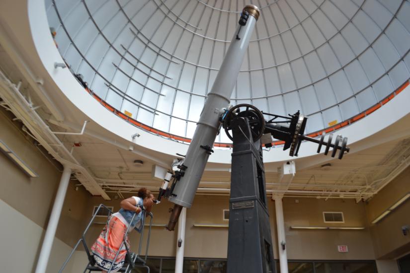 Individual standing on a ladder looking through the Alvan Clark telescope