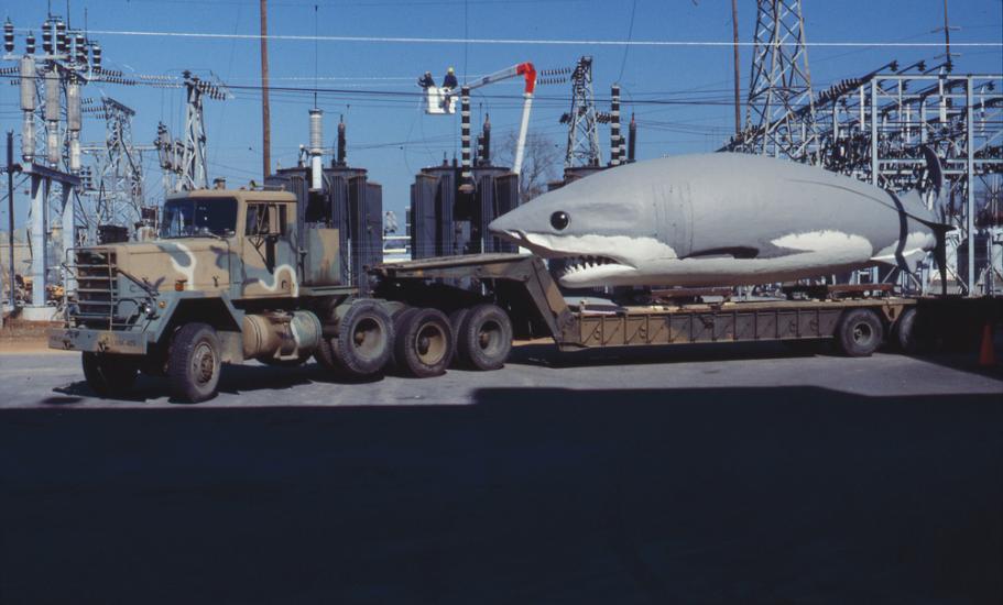 Giant Megalodon replica sits on the back on a National Guard flatbed truck in a parking area