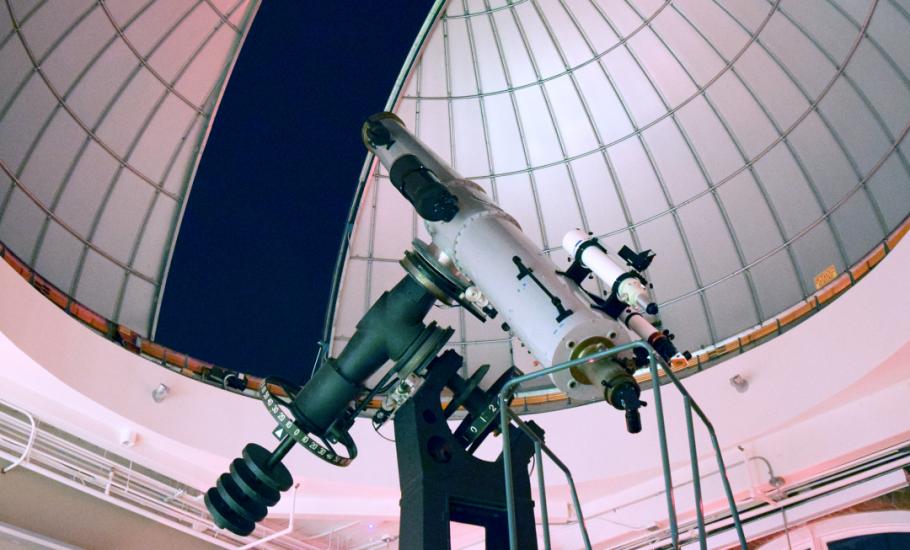 Large white telescope points towards the dark night sky under a partially open observatory