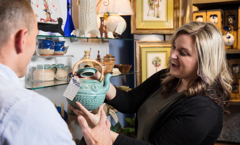 Blonde woman holds up light green ceramic tea pot on sale in the museum store