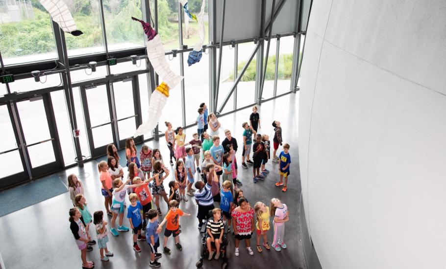 Looking down on a group of students standing in the planetarium lobby with paper mobile artwork hanging from ceiling