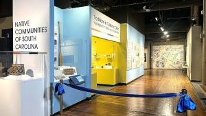 Wall that reads&amp;quot; Native Communities of South Carolina.&amp;quot; Several display cases are visible as well as bright yellow alcove with a sign above that reads: Traditions in Catawba Clay