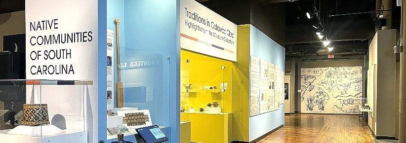 Wall that reads" Native Communities of South Carolina." Several display cases are visible as well as bright yellow alcove with a sign above that reads: Traditions in Catawba Clay