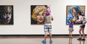 Family looks at 3 pieces of art displayed on a wall, including a portrait of Marilyn Monroe